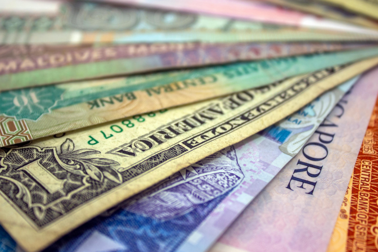 Close-up of assorted international banknotes from multiple countries arranged in a fan-like spread, showing varied colours, designs, and denominations.