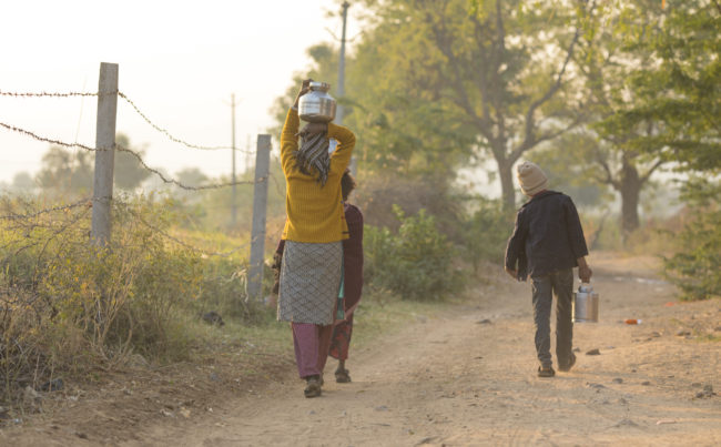 woman carrying water on unpaved road in India