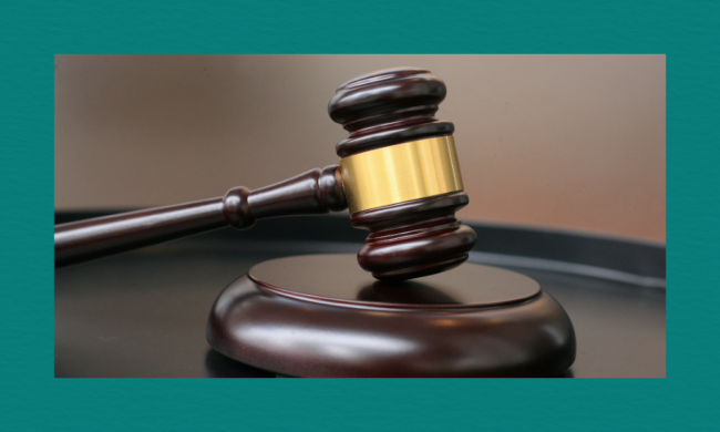 A close-up of a judge’s dark wooden gavel with a gold band resting on a sound block, set against a softly blurred background.