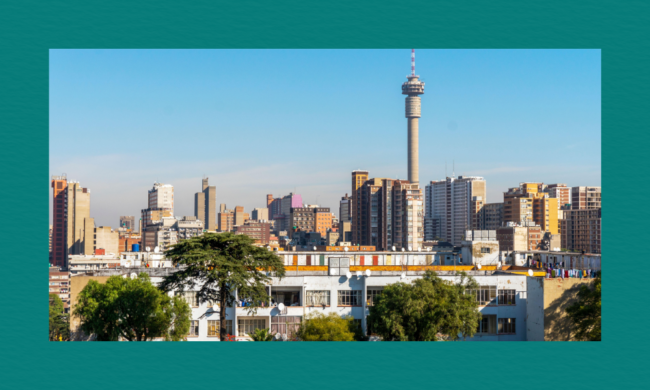 “A transparent system, run by people without integrity, is equally corrupt”: Municipal officials dissect issues of corruption and integrity in South Africa’s urban development processes A cityscape with dense high‑rise buildings under a clear blue sky, featuring a tall telecommunications tower with a circular observation deck. Shorter residential buildings with satellite dishes and laundry appear in the foreground, partially framed by green trees.