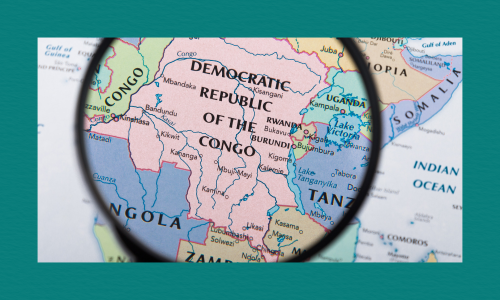 Close‑up of a map of Central Africa with a magnifying glass highlighting the Democratic Republic of the Congo, showing surrounding countries and nearby major cities.