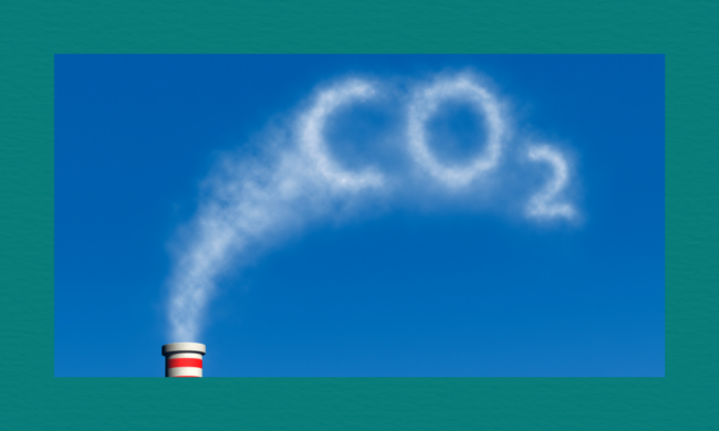 Factory smokestack releasing white smoke that forms the letters “CO₂” against a clear blue sky.