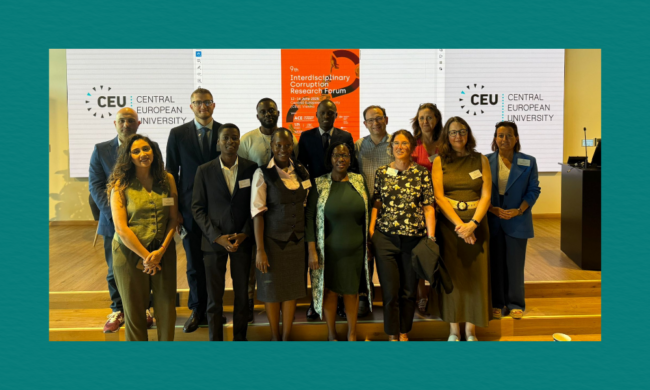 A group of conference participants stand together on a wooden stage in front of a backdrop displaying the Central European University logo, with a bright orange poster behind them announcing the 9th Interdisciplinary Corruption Research Forum held in June 2023 in Budapest.