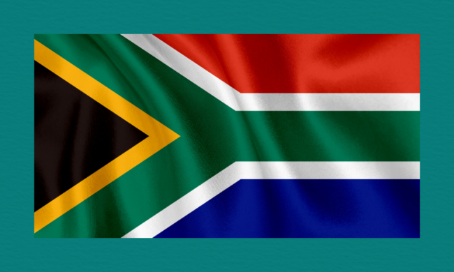 South Africa’s national flag with its distinctive green Y‑shape, black triangle, and red, blue, yellow, and white colour blocks, shown against a teal background with visible fabric folds.