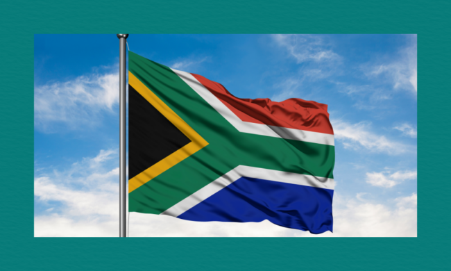 A South African flag waves on a tall flagpole against a bright blue sky with scattered clouds.