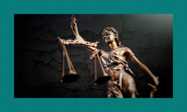 A bronze statue of Lady Justice stands against a dark textured background, showing the blindfolded figure holding a set of balanced scales, her metallic surface highlighted by dramatic lighting.