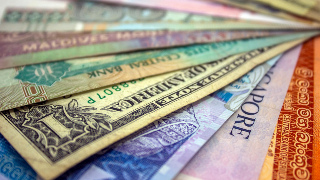 Close-up of assorted international banknotes from multiple countries arranged in a fan-like spread, showing varied colours, designs, and denominations.