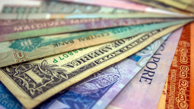 Close-up of assorted international banknotes from multiple countries arranged in a fan-like spread, showing varied colours, designs, and denominations.