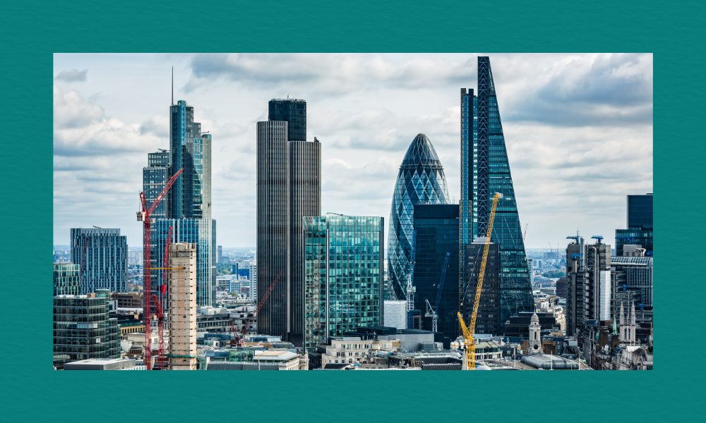 A view of London’s skyline featuring the Gherkin, the Cheesegrater, and other modern skyscrapers, with several construction cranes visible among the buildings. Older stone architecture sits in the foreground beneath a partly cloudy sky.