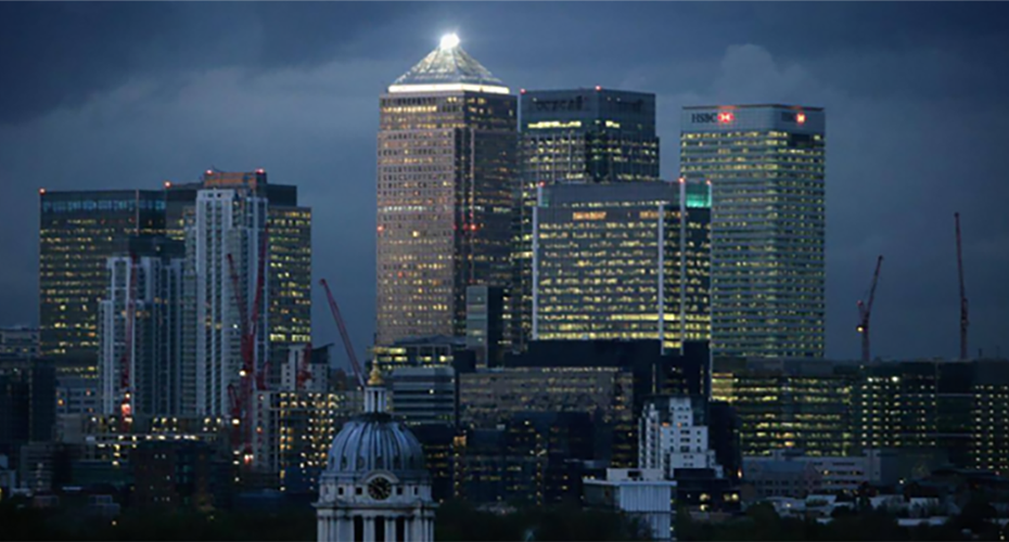 Kleptocracy-resized Evening view of the Canary Wharf skyline with One Canada Square lit at the top, surrounded by illuminated HSBC and Citi towers, red construction cranes, and a domed historic building in the foreground.