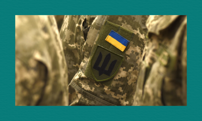 A close-up of a Ukrainian military uniform sleeve featuring two patches — a blue‑and‑yellow Ukrainian flag above a dark trident emblem, both sewn onto a camouflage fabric.
